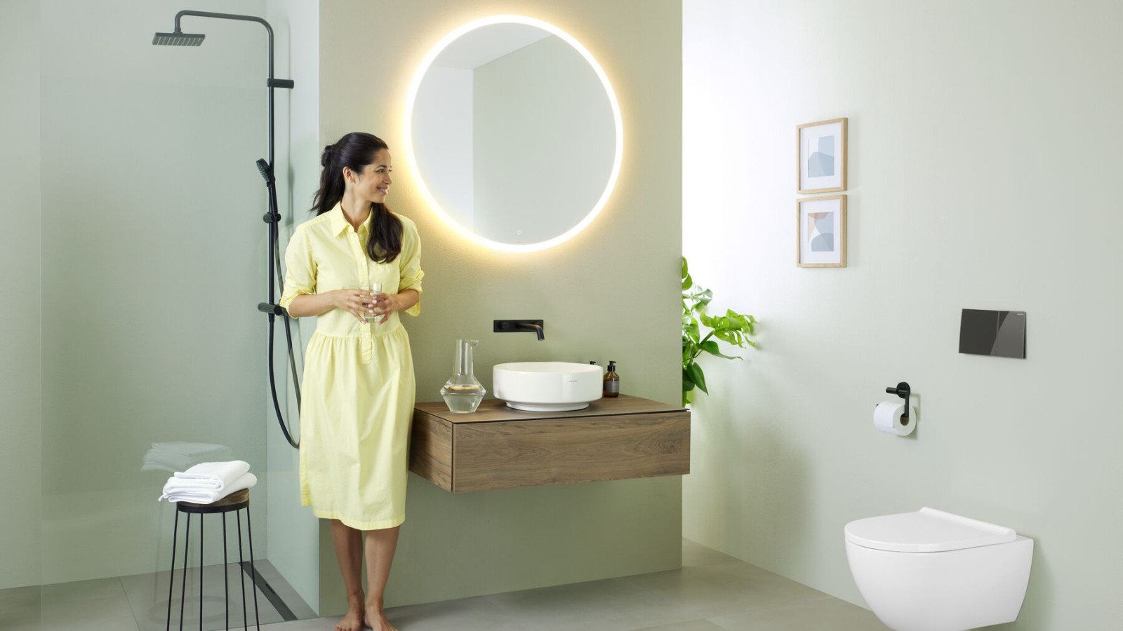 Woman in yellow dress standing in front of mint green bathroom with furniture and bathroom ceramics from Geberit and black taps. Woman in yellow dress standing in front of mint green bathroom with furniture and bathroom ceramics from Geberit and black taps.