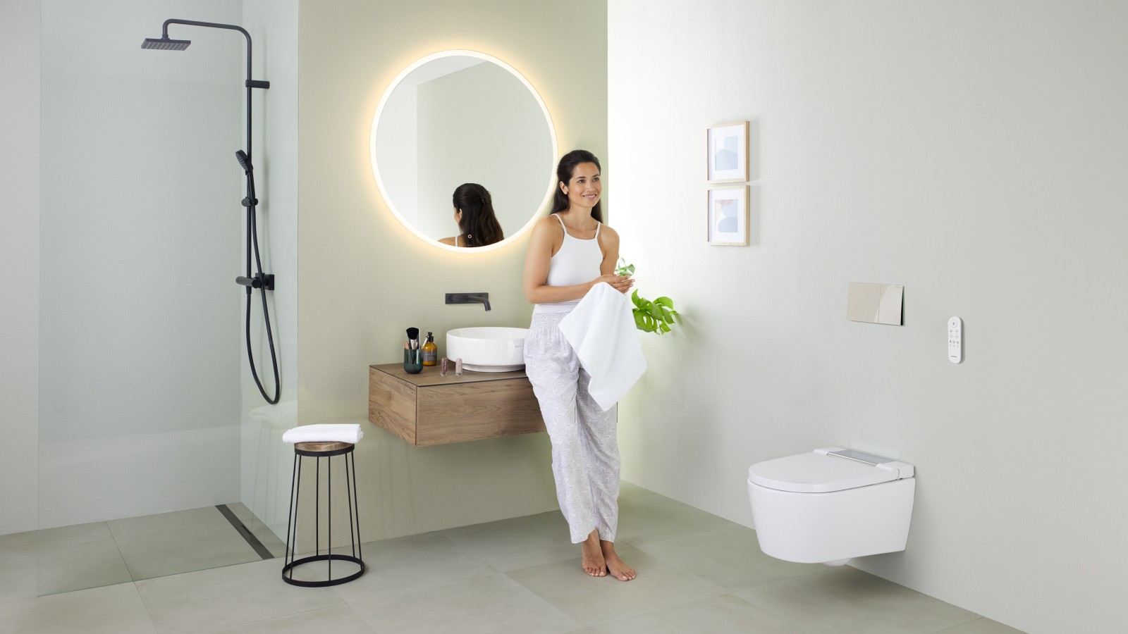 Woman leaning on a washbasin in a bathroom with Geberit AquaClean Sela shower toilet and Geberit VariForm washbasin and furniture Woman leaning on a washbasin in a bathroom with Geberit AquaClean Sela shower toilet and Geberit VariForm washbasin and furniture