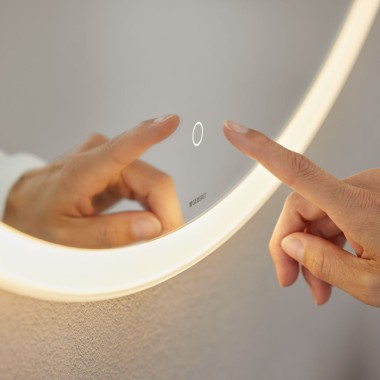 Hand operating touch sensor switch on Geberit Option Round mirror (© Geberit)