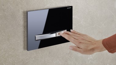 Hand triggers a flush on the black actuator plate Sigma50 (© Geberit)