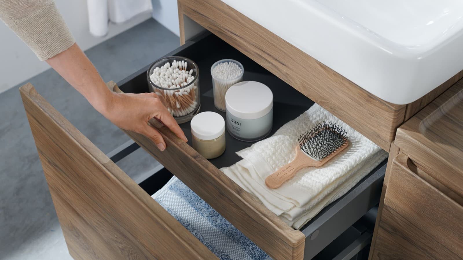 A hand opens one of the drawers of the Geberit Selnova washbasin cabinet in a natural design A hand opens one of the drawers of the Geberit Selnova washbasin cabinet in a natural design